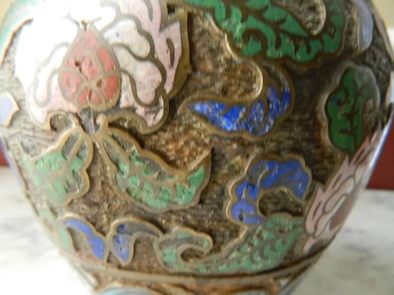 K&ouml;nnte beinhalten: Eine runde, braune Keramikvase mit floralem Design. Die Vase ist mit gr&uuml;nem, blauem und rosa Email verziert. Die Vase hat eine strukturierte Oberfl&auml;che.