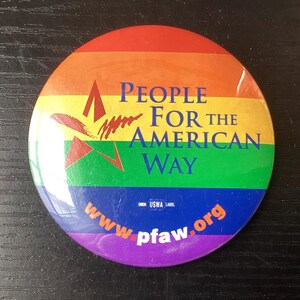May include: A round button with a rainbow gradient background. The button features the text "PEOPLE FOR THE AMERICAN WAY" in white and the website "www.pfaw.org" in orange. The button also has a red and green graphic.