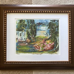 May include: Framed art print of a landscape scene with a house, trees, and flowers. The print is in a brown wooden frame with a white mat. The artwork is signed and numbered 10/200. The text "Gulf Coast Light" is visible.