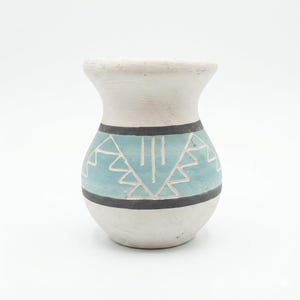 May include: A small, off-white ceramic vase with a rounded body and a flared rim. The vase features a turquoise band with geometric designs, bordered by black lines. The overall design is simple and elegant.