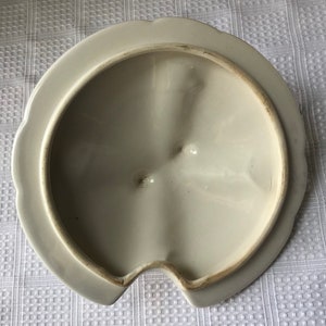 May include: White ceramic lid with a scalloped edge and a small spout. The inside of the lid has a smooth, white finish.