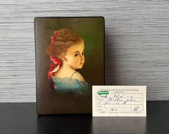 May include: A small, rectangular wooden box with a hinged lid. The lid features a painted portrait of a young girl with a pink ribbon in her hair. The girl is wearing a blue dress and looking to the right. The box has a label on the front that reads "Короб - 2".
