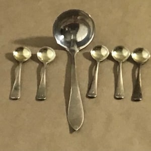 May include: A set of seven silver spoons, including a large serving spoon and six smaller spoons. The spoons are all polished and shiny.