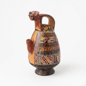 May include: A ceramic vessel with a handle and a spout, featuring a detailed animal head at the top. The vessel is adorned with geometric patterns in shades of brown, black, yellow, and red. The design suggests an ancient or tribal aesthetic.