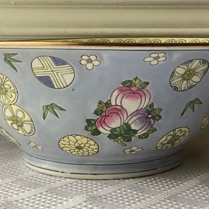 May include: A large, light blue porcelain bowl with a gold rim. The bowl is decorated with a floral pattern in shades of pink, yellow, and green. The bowl is perfect for serving fruit, salads, or other dishes.