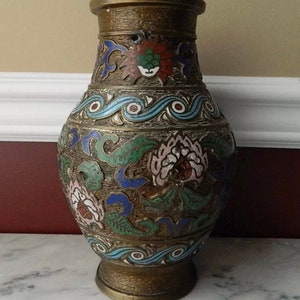 K&ouml;nnte beinhalten: Eine Messingvase mit einem Cloisonn&eacute;-Emaille-Design. Die Vase ist mit floralen und Wellenmustern in Blaut&ouml;nen, Gr&uuml;n, Rot und Wei&szlig; verziert.