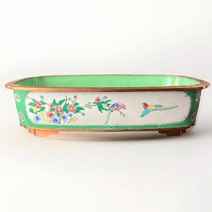 May include: A rectangular green and white planter with a floral and bird design. The planter has a copper rim and three small feet.
