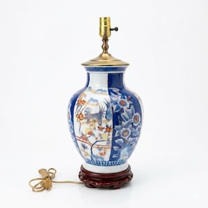 May include: A decorative ceramic table lamp with a blue, white, and gold floral design. The lamp has a brass neck and a wooden base. The lamp's design features a blue and white floral pattern with a gold accent.