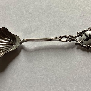 May include: A silver spoon with a shell-shaped bowl and a decorative handle. The handle features a white shield with a black bear and the word "BERLIN".