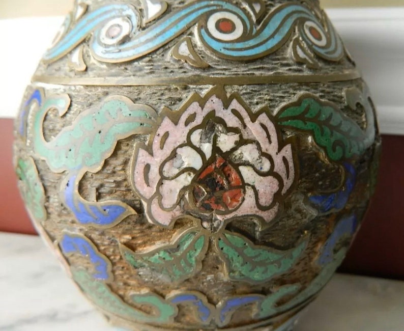 K&ouml;nnte beinhalten: Eine vintage Cloisonn&eacute;-Vase mit floralem Design. Die Vase ist mit blauem, gr&uuml;nem, wei&szlig;em und rotem Email verziert. Die Vase ist aus Metall und hat eine strukturierte Oberfl&auml;che.