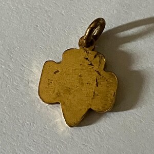May include: A gold-colored pendant in the shape of a trefoil, with a small loop at the top for a chain. The pendant has a slightly worn appearance, suggesting it is vintage or antique. The trefoil shape is a classic symbol.