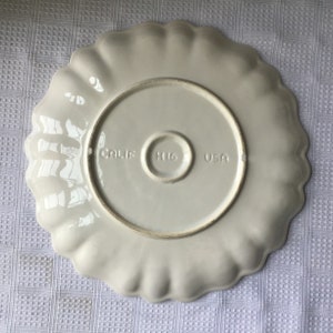 May include: White ceramic serving plate with a scalloped edge. The bottom of the plate has the words "CALIF. HI6 USA" printed on it.