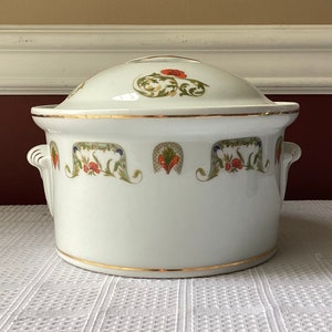 May include: White porcelain casserole dish with a lid. The dish has a gold trim and a floral design with red, green, and blue accents.