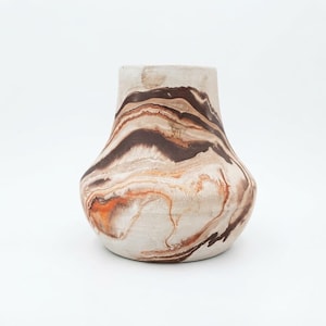 May include: A wide-based vase with a tapered neck, featuring a marbled pattern of cream, dark brown, and burnt orange swirls. The surface has a matte, textured appearance with fluid, organic lines wrapping around the entire body of the vessel.