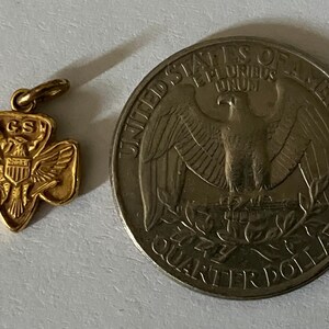 May include: A gold-colored Girl Scout pendant with the letters "GS" and an eagle emblem, next to a United States quarter coin. The coin features an eagle and the words "Quarter Dollar".