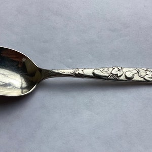May include: A silver spoon with an ornate design of leaves and grapes on the handle.