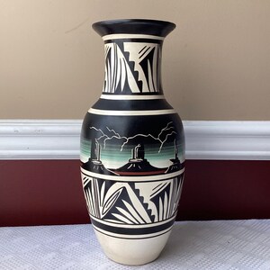 May include: A black and white ceramic vase with a Southwestern design. The vase features a landscape scene with mountains and lightning bolts. The vase is approximately 12 inches tall.