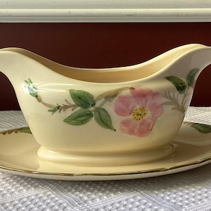 May include: A white ceramic gravy boat with a pink rose and green leaves design. The boat has a matching saucer.