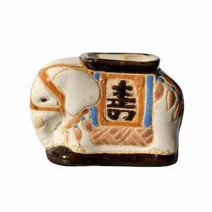 May include: A ceramic elephant figurine in white, brown, orange, and blue. The elephant has a rectangular opening on its back and a decorative pattern with Chinese characters. The figurine is a decorative item.