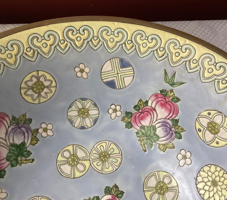 May include: A large, round, blue and white ceramic bowl with a yellow rim and intricate floral and geometric designs. The bowl features a variety of flowers, leaves, and stylized patterns.