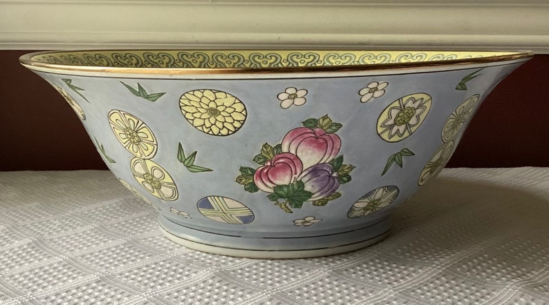 May include: A large, blue and white porcelain bowl with a gold rim. The bowl is decorated with a floral pattern and a fruit motif.