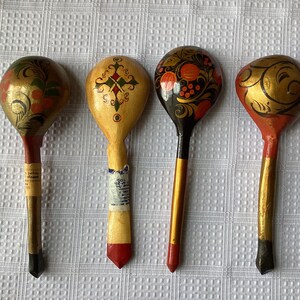 May include: Four wooden spoons with hand-painted designs. The spoons are decorated with floral patterns, geometric shapes, and gold accents. The spoons are all different colours, including red, black, and gold.