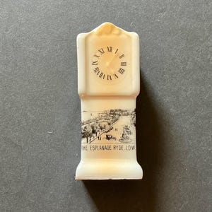 May include: A small, off-white souvenir clock-shaped figurine. The clock face displays Roman numerals. The base features a black and white illustration of a seaside promenade with the text "THE ESPLANADE RYDE I.O.W."