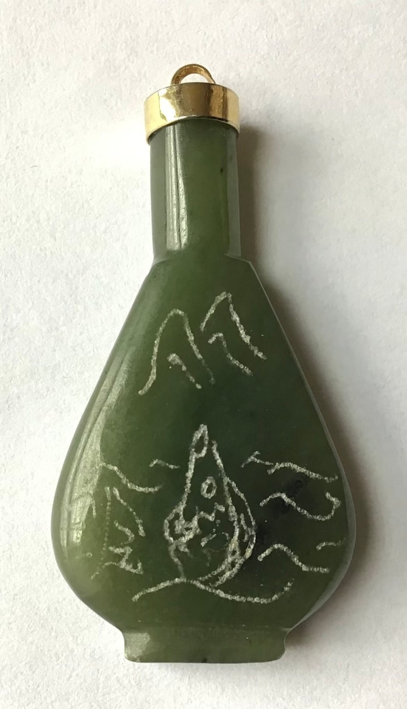 May include: A green jade pendant in the shape of a bottle with a gold top. The bottle has a white design of mountains and waves.