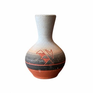 May include: A small, handcrafted vase with a unique design. The vase features a light gray neck that transitions to a body with a gradient of colors, including orange, black, and red. The vase has a tribal-inspired pattern.