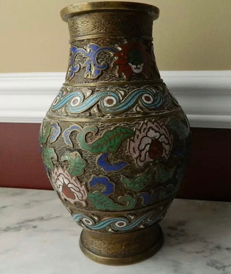 K&ouml;nnte beinhalten: Eine Messingvase mit Cloisonn&eacute;-Design. Die Vase ist mit floralen und Wellenmustern in Blaut&ouml;nen, Gr&uuml;n, Rosa und Rot verziert.