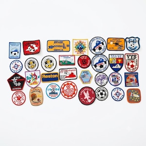 May include: A collection of various embroidered soccer patches in diverse shapes, colors, and sizes. The patches feature team names, logos, soccer balls, and text such as Braddock Road Youth Club, Virginia, Atlee Arsenal, VYS, Reston, and Annandale Falcons.