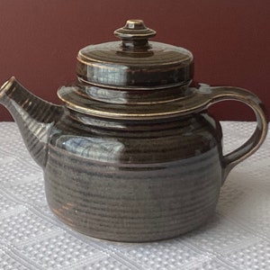 May include: A brown ceramic teapot with a lid and a striped pattern. The teapot has a spout and a handle.