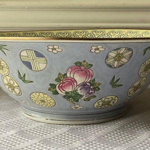 May include: A large, blue and white porcelain bowl with a gold rim. The bowl is decorated with a floral pattern and a cluster of pink and purple fruit.