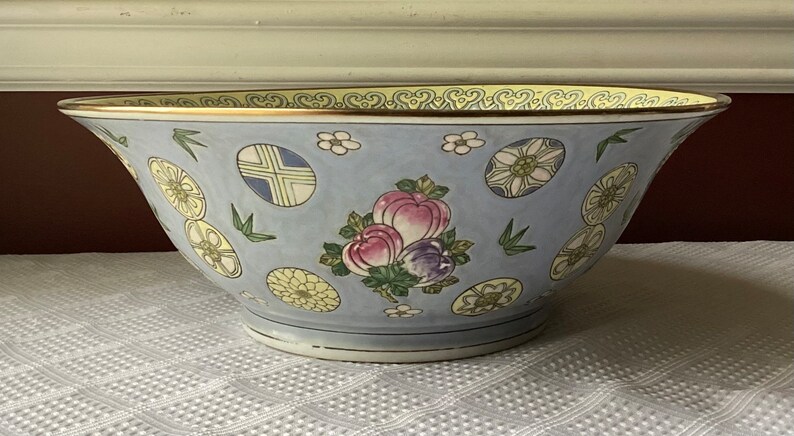 May include: A large, blue and white porcelain bowl with a gold rim. The bowl is decorated with a floral pattern and a cluster of pink and purple fruit.
