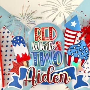 May include: Red, white, and blue cake topper with the words "Red White & Two Aiden" and a firework, ice cream cone, and cupcake design.