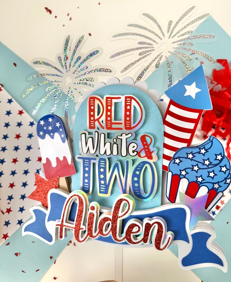 May include: Red, white, and blue cake topper with the words "Red White & Two Aiden" and a firework, cupcake, and popsicle design.
