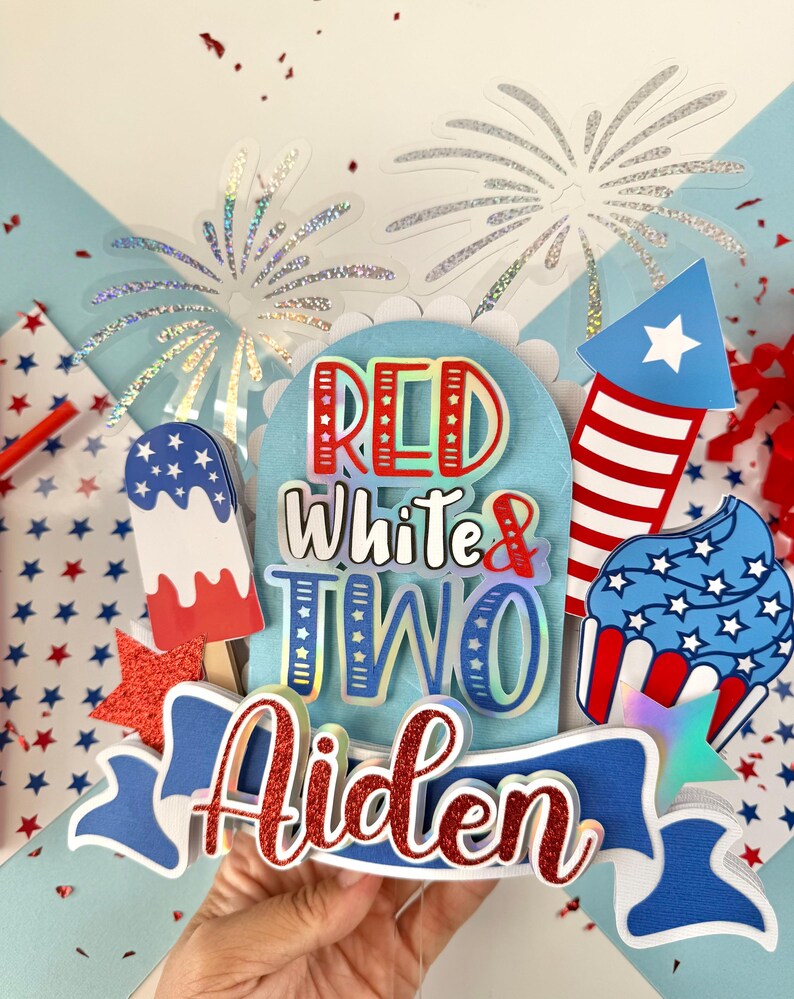 May include: Red, white, and blue cake topper with the words "Red White & Two Aiden" and a firework, cupcake, and popsicle design.