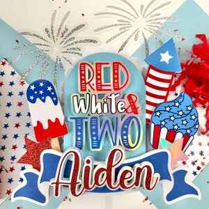 May include: Red, white, and blue cake topper with the words "Red White & Two" and the name "Aiden". The topper features a firework, a cupcake, and an ice cream pop.