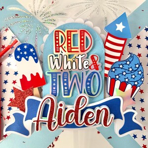 May include: Red, white, and blue cake topper with the words "Red White & Two Aiden" and a firework, cupcake, and popsicle design.