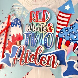May include: Red, white, and blue cake topper with the words "Red White & Two" and the name "Aiden" in red glitter. The topper also features a firework, a cupcake, and an ice cream cone.