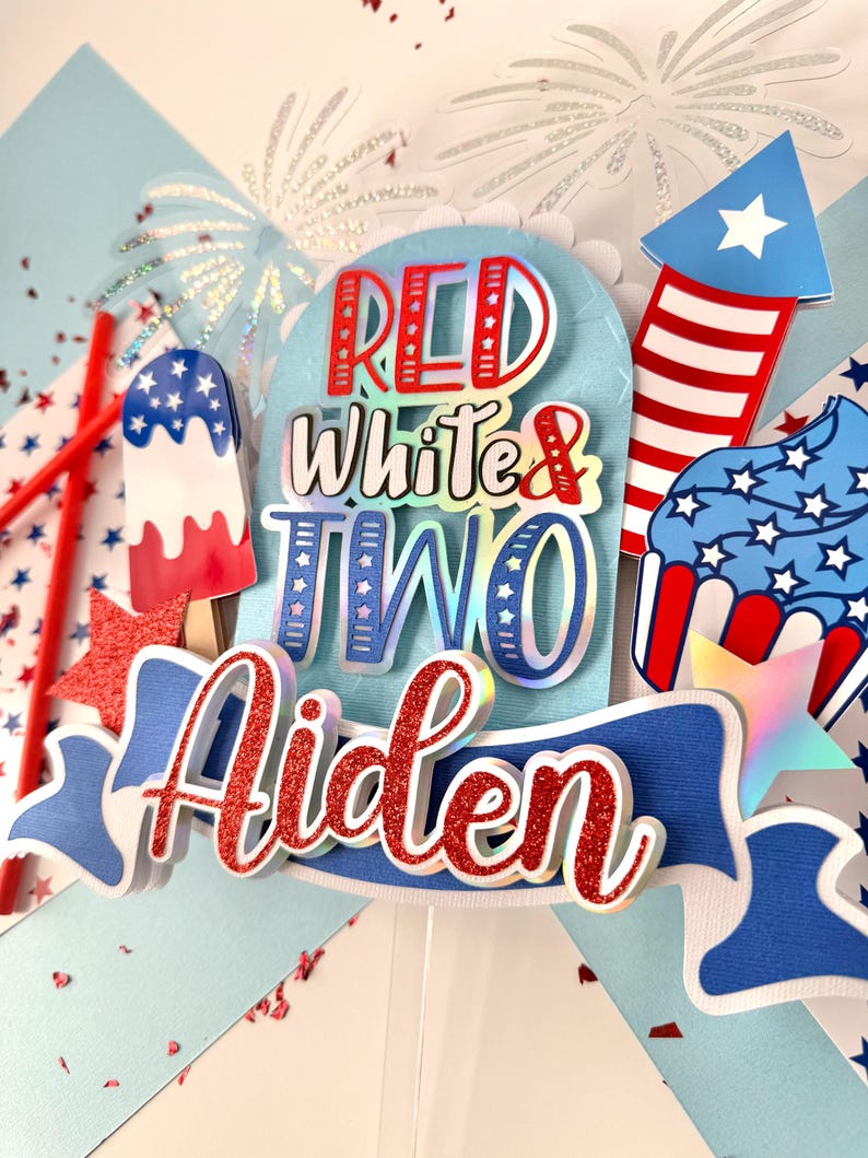 May include: Red, white, and blue cake topper with the words "Red White & Two" and the name "Aiden" in red glitter. The topper also features a firework, a cupcake, and an ice cream cone.