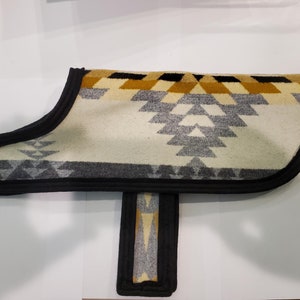 Könnte beinhalten: Ein Hunde-Mantel mit weißem, grauem und goldenem Muster und schwarzem Besatz. Der Mantel hat ein geometrisches Design und ist aus einem weichen, bequemen Material gefertigt.