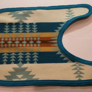 Op de afbeelding: Een turquoise blauwe stof met een geometrisch patroon in wit. De stof heeft een turquoise blauwe rand.