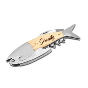 May include: A fish-shaped multi-tool with a wooden handle and stainless steel components. The tool includes a corkscrew, bottle opener, and knife. The word "Serenity" is engraved on the wooden handle.