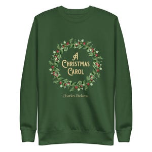 Puede incluir: Sudadera verde oscuro con un diseño de corona de hojas verdes y bayas rojas. El texto "A Christmas Carol" está en el centro, con "Charles Dickens" debajo. La sudadera es de manga larga y cuello redondo.