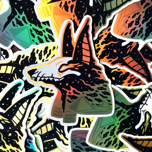 Pu&ograve; includere: Un mucchio di adesivi colorati con un'illustrazione in bianco e nero di uno scheletro di animale su uno sfondo stellato. Lo scheletro &egrave; circondato da fiamme e ha un motivo geometrico.