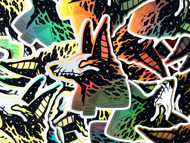 Pu&ograve; includere: Un mucchio di adesivi colorati con un'illustrazione in bianco e nero di uno scheletro di animale su uno sfondo stellato. Lo scheletro &egrave; circondato da fiamme e ha un motivo geometrico.