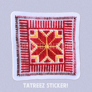 May include: A red and yellow cross-stitch design on a white background. The design is framed by a red border. The sticker says "TATREEZ STICKER!"