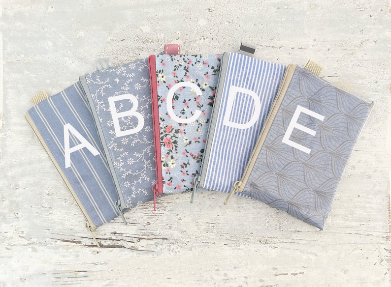 May include: Five zippered pouches with different patterns and colors. Each pouch has a letter printed on it, spelling out the word "ABCDE".