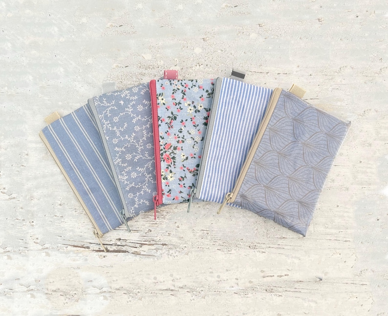 May include: Five different fabric pencil cases with various patterns. The cases are all blue and white with different patterns, including floral, stripes, and geometric designs.